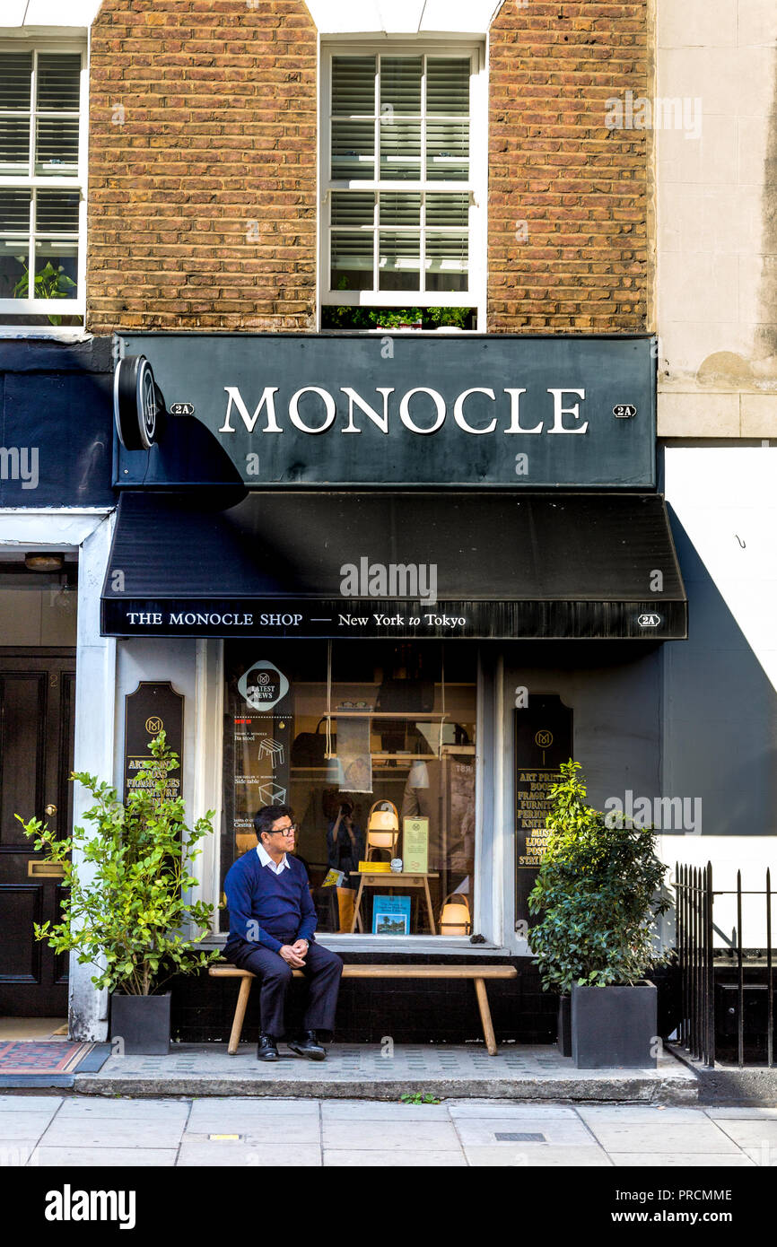 Un uomo seduto su una panchina al di fuori di un negozio, Monoclasse Shop, London, Regno Unito Foto Stock