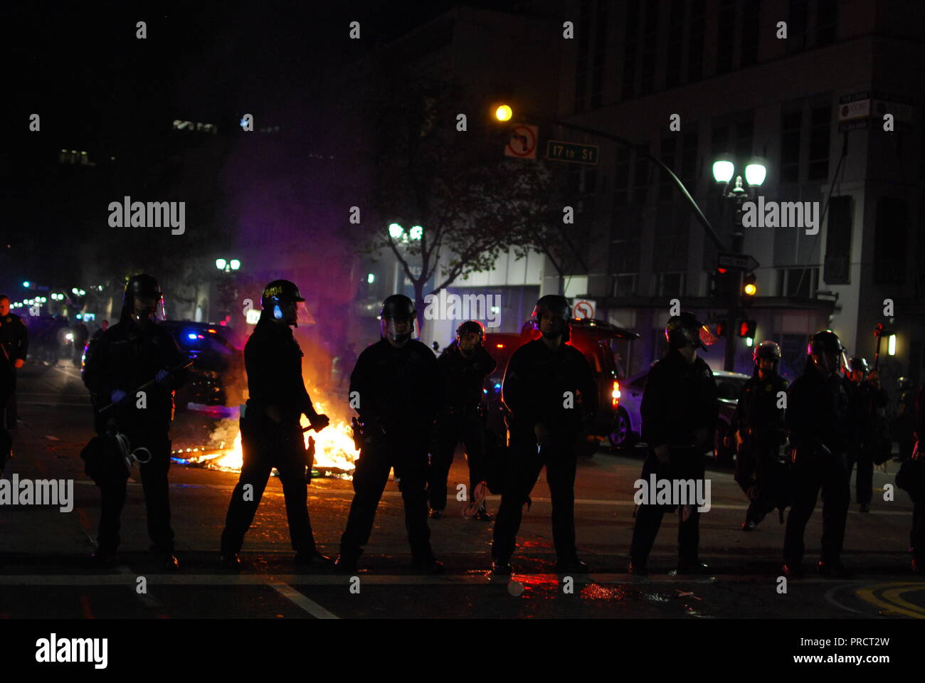 Oakland poliziotti marzo davanti ad un fuoco che arde su Broadway durante le proteste contro l elezione del presidente Donald Trump su nov. 9, 2016. Foto Stock