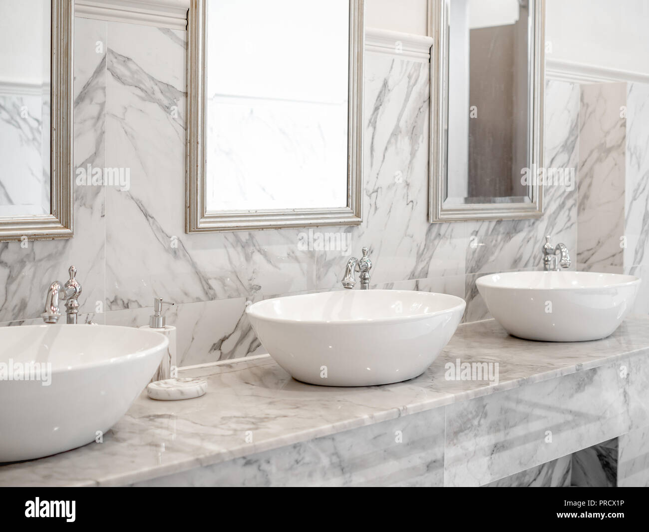 Bianco dissipatore di lusso in bagno. White design interno moderno bagno in marmo con tre round lavabo, alluminio rubinetti e specchi sul muro. Foto Stock