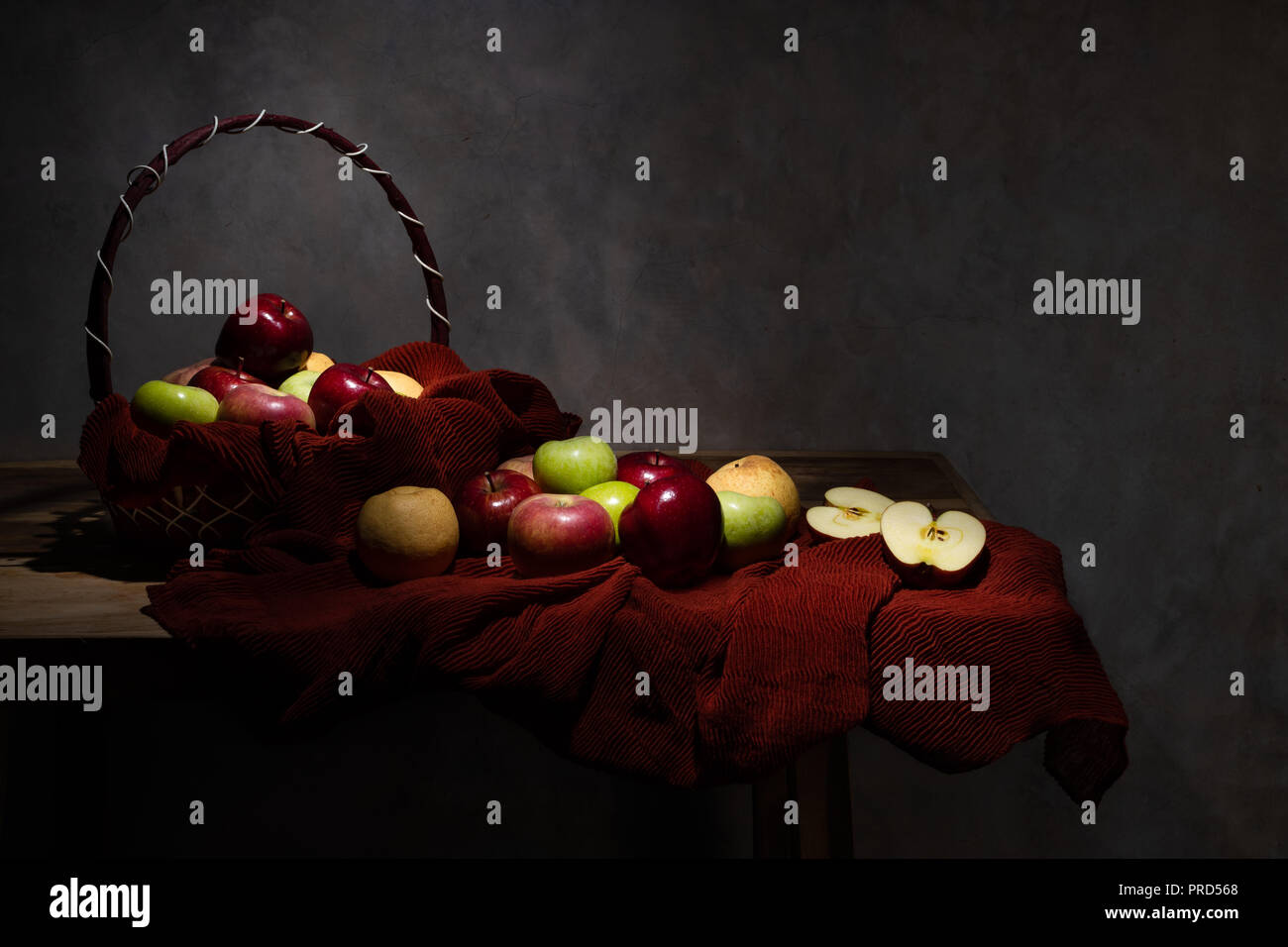 Basketful di vario tipo di apple con alcuni sul tavolo di legno e uno di loro è tagliato a metà Foto Stock
