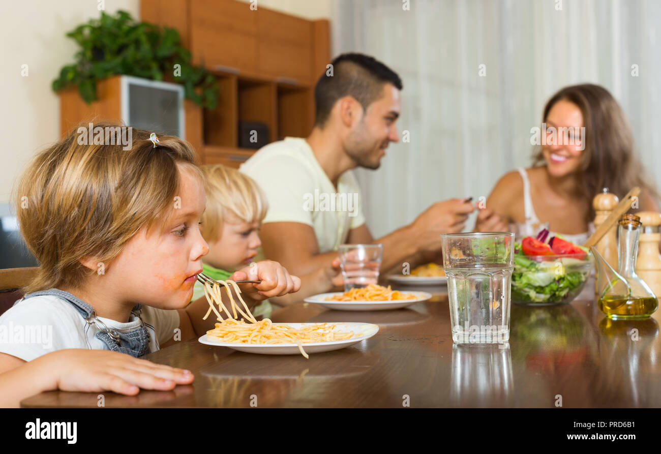 Famiglia sorridente con due piccole figlie di mangiare con gli spaghetti in tavola. Focus sulla ragazza Foto Stock