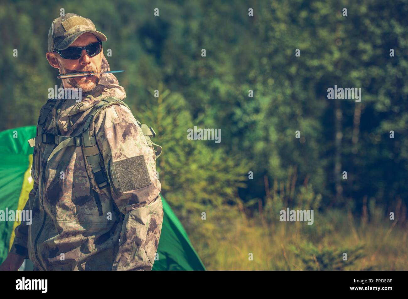 Gli uomini e le selvagge. Uomini caucasici nella sua 30s indossare abbigliamento Camouflage con grande piscina coltello in bocca. Foto Stock
