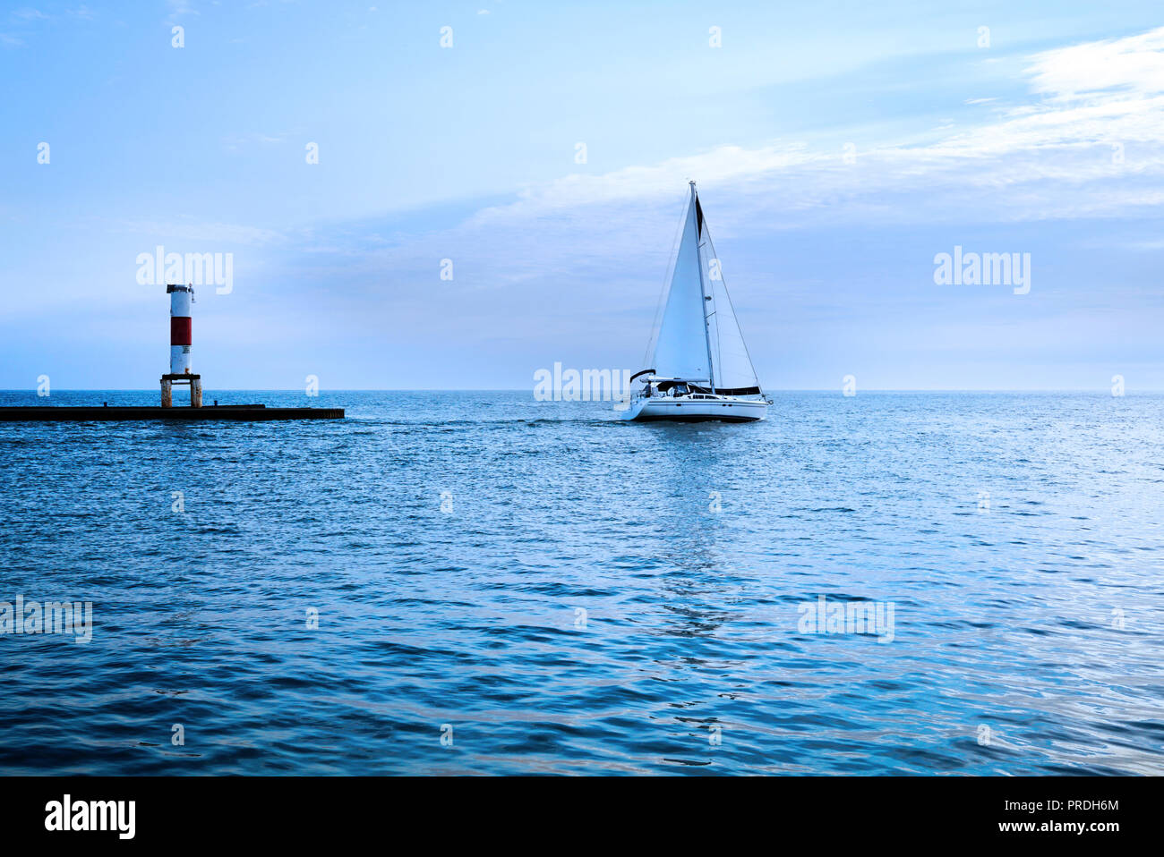 Yacht al tramonto con il blu del mare. Bianca vela contro lo sfondo di un faro e mare orizzonte va verso il tramonto. Dietro la nave è una luce Foto Stock