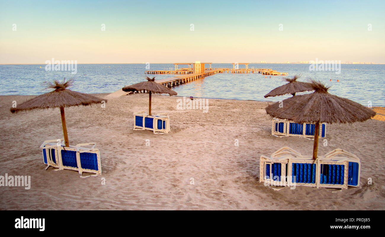Naturale ombrelloni di paglia su una spiaggia deserta con largo molo di andare in mare, bagnata dal caldo sole serale - spazio per il testo Foto Stock