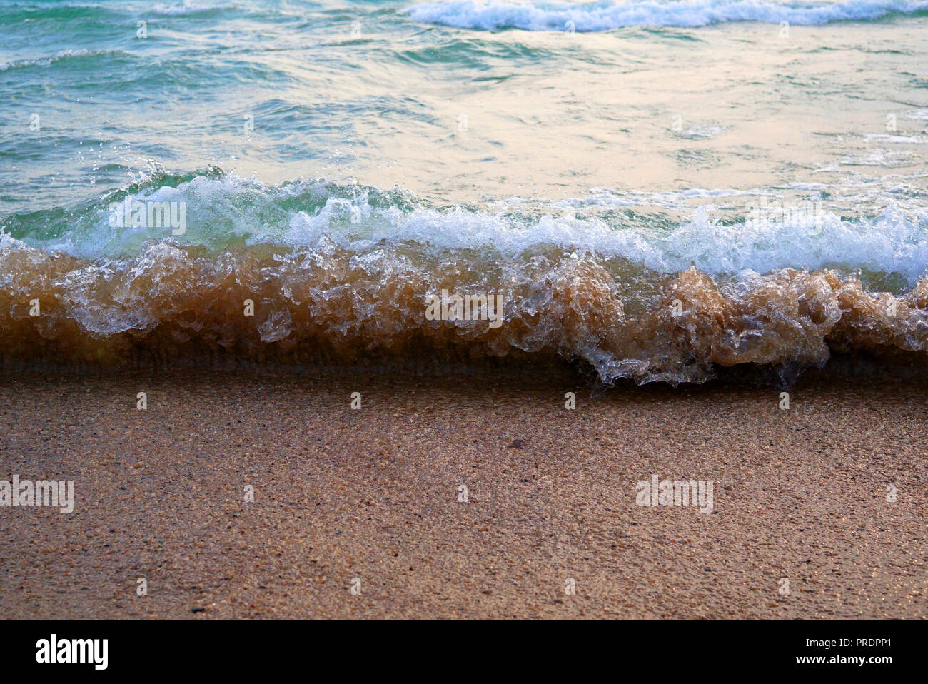 Un onda tricolore corre sopra la sabbia come un piccolo Tsunami. Bella pura acqua e schiuma bianca sulla cresta. Bolle d'aria e acqua bollente afferrato sabbia e li Foto Stock