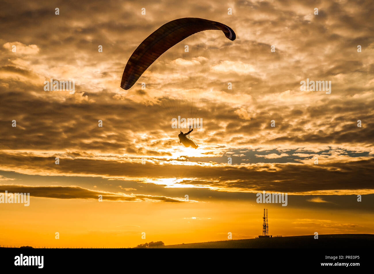 Firle Beacon, Lewes, East Sussex, Regno Unito. 1° ottobre 2018..i Paragliders si sono ssilhouette contro il sole che si staglia sotto la copertura del cloud di Altocumulus. Volare sul sito nel South Downs è stato possibile solo per un breve periodo intorno al tramonto, come il forte vento gustosissimo dal Nord Ovest calmato a condizioni di volo sicuro. Foto Stock