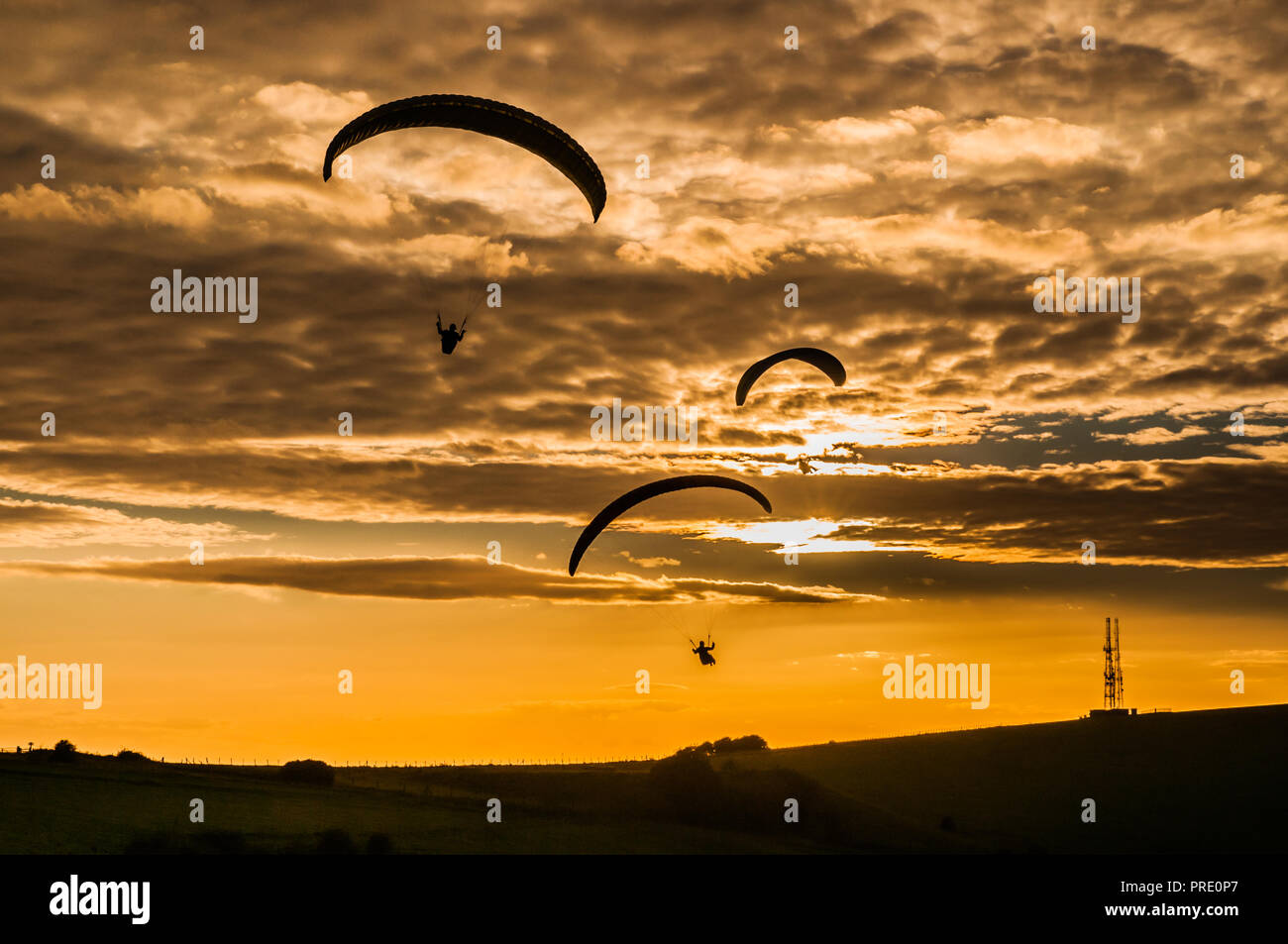 Firle Beacon, Lewes, East Sussex, Regno Unito. 1° ottobre 2018..i Paragliders si sono ssilhouette contro il sole che si staglia sotto la copertura del cloud di Altocumulus. Volare sul sito nel South Downs è stato possibile solo per un breve periodo intorno al tramonto, come il forte vento gustosissimo dal Nord Ovest calmato a condizioni di volo sicuro. Foto Stock