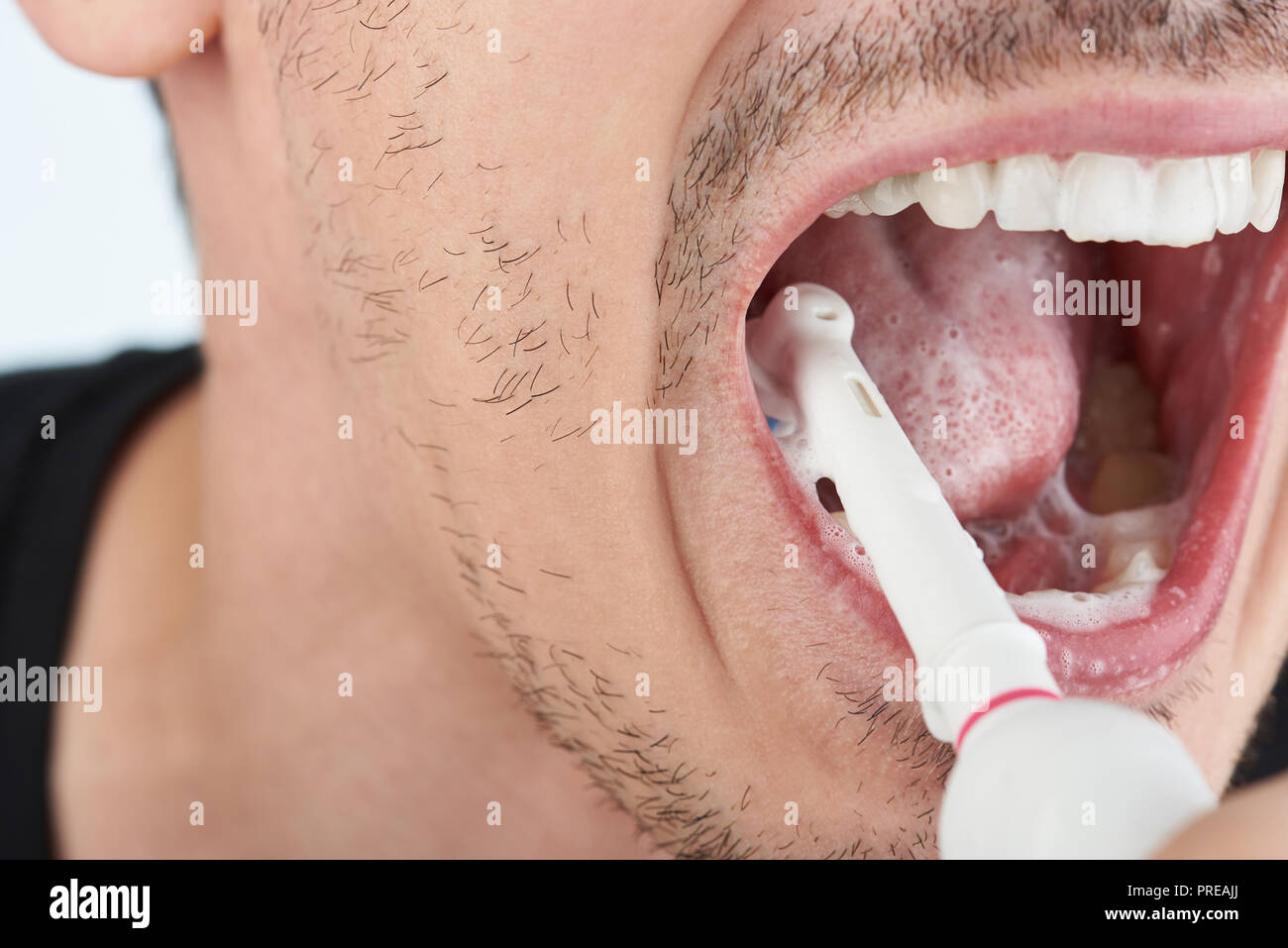 L'uomo spazzolare i denti con spazzolino elettrico vista ravvicinata Foto Stock