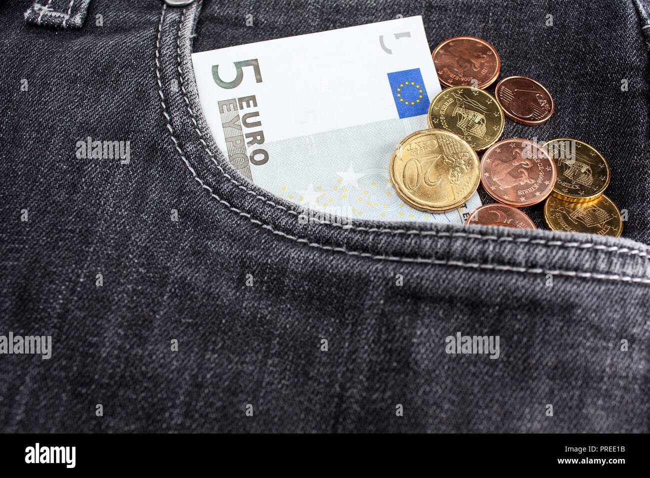 Una banconota di cinque euro e un sacco di monete si trovano nella parte anteriore della tasca dei jeans neri Foto Stock