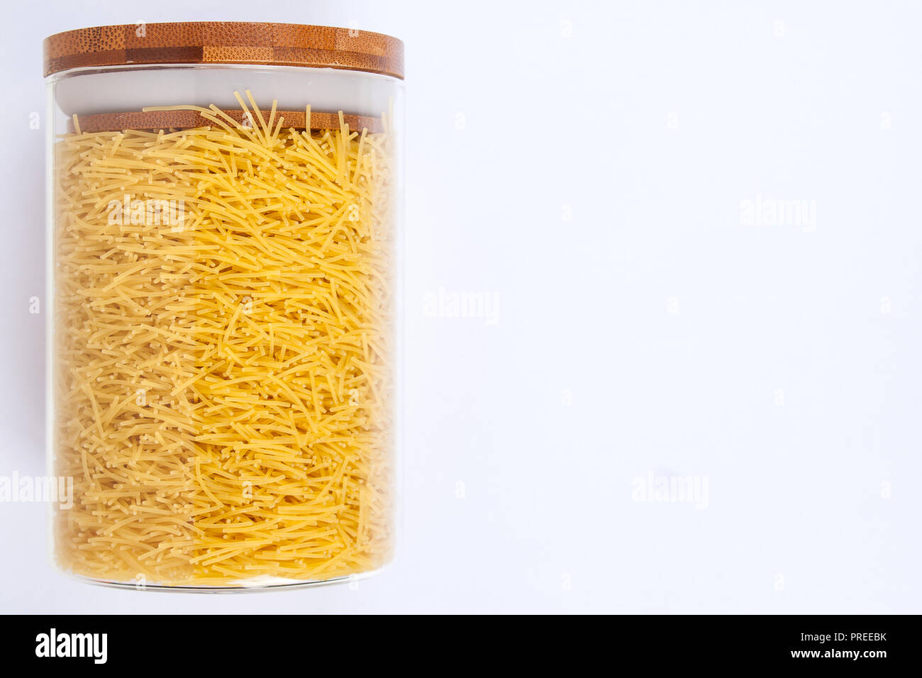 Vaso di vetro con un coperchio di legno all'interno di vermicelli o la pasta su uno sfondo bianco. Vista dall'alto. Foto Stock