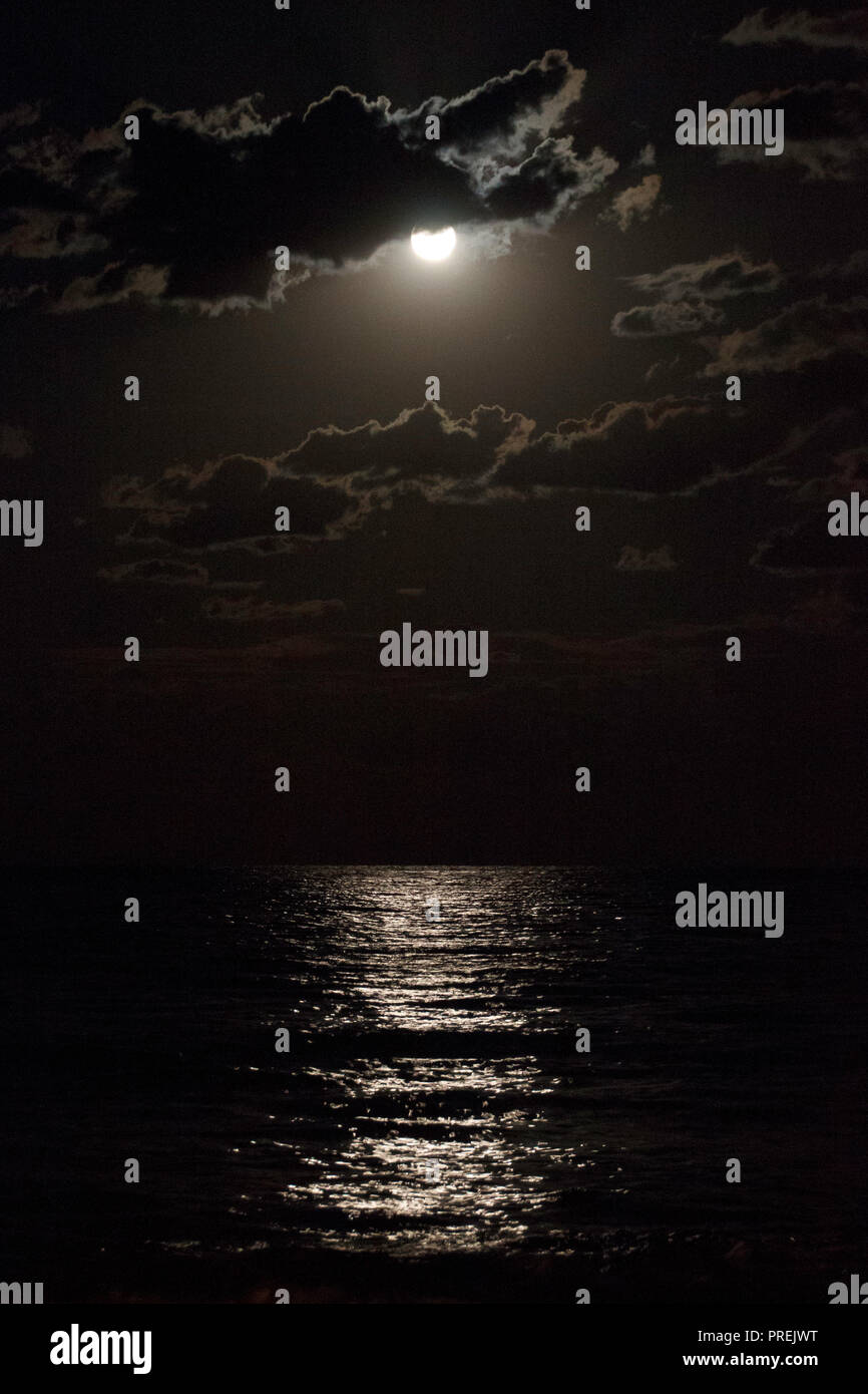 La luna piena in un nuvoloso cielo notturno che riflette i raggi della luna sul mare, visualizzazione verticale Foto Stock