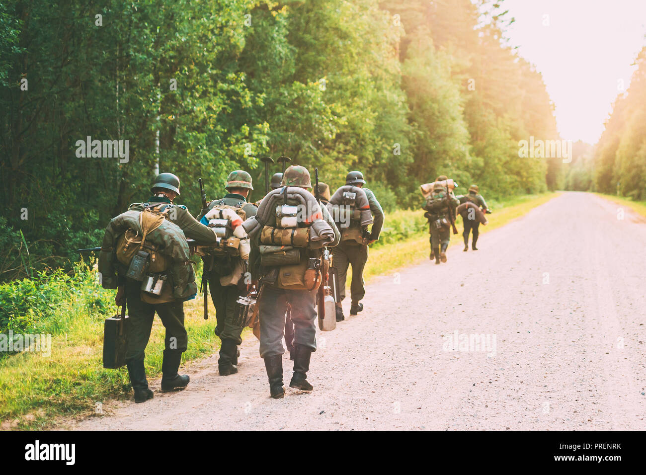 Re-enactors vestito come tedesco Soldato di fanteria nella guerra mondiale II marciando a piedi lungo la strada forestale in serata d'estate. Tramonto Foto Stock