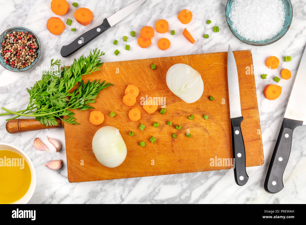 Tempo di preparazione o di mise en place. Un overhead foto professionali dei coltelli chef, ripresa dall'alto su un tagliere con un trito di verdure e spezie, su un marmo Superficie di cottura Foto Stock
