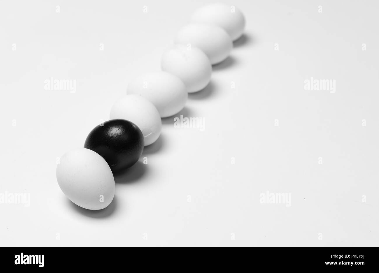 Su uno sfondo bianco, a pochi le uova bianche uno nero che simboleggia la diversità, separazione e leadership Foto Stock