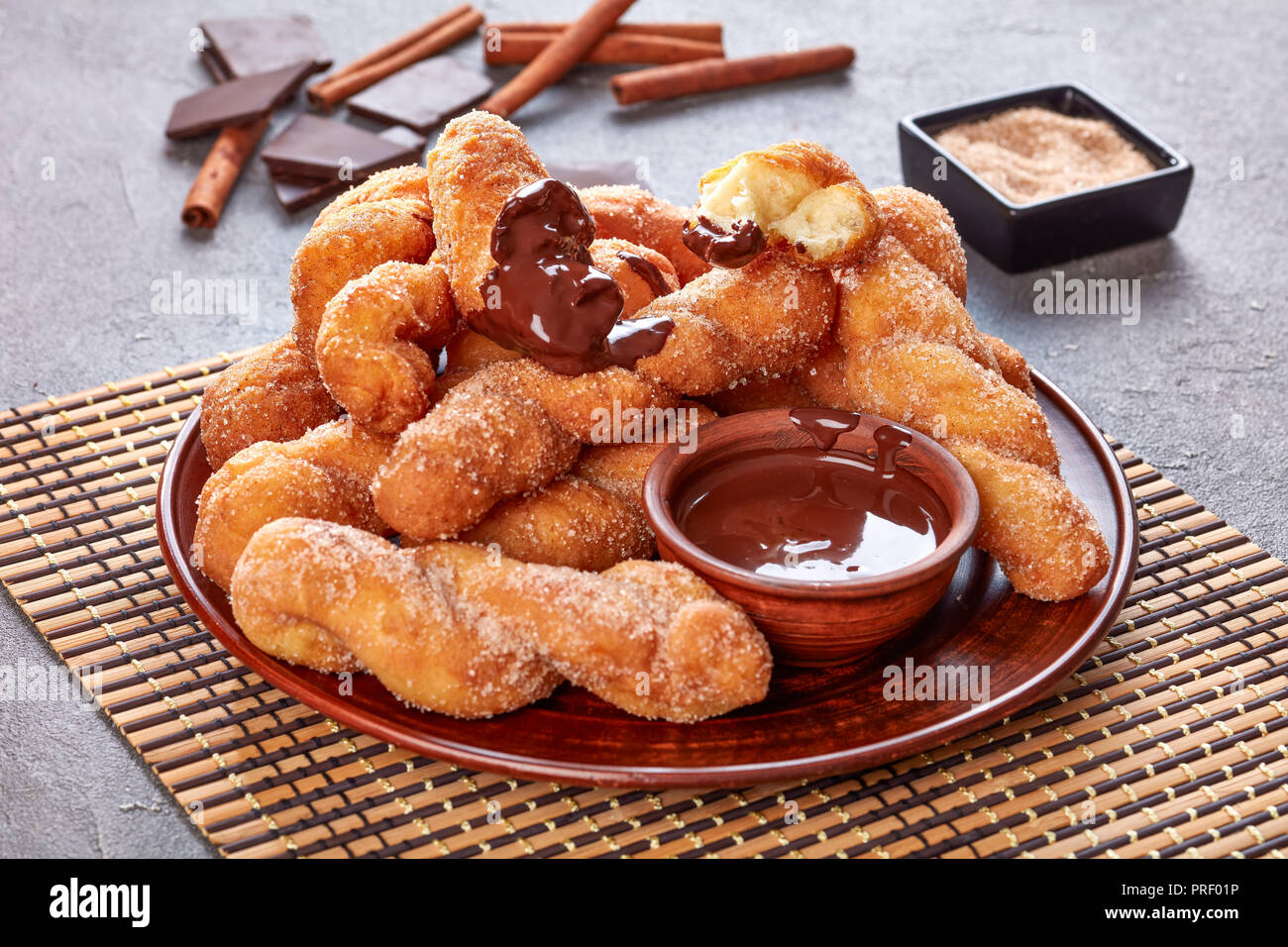 Ritorto ciambelle coreano - Kkwabaegi spolverati con zucchero e servito con salsa di cioccolato su un piatto di terracotta e su un tappetino di bambù. barra di cioccolato, cannella st Foto Stock
