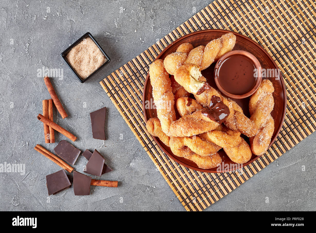 Ritorto ciambelle coreano - Kkwabaegi spolverati con zucchero e servito con salsa di cioccolato su un piatto di terracotta e su un tappetino di bambù. barra di cioccolato, cannella st Foto Stock