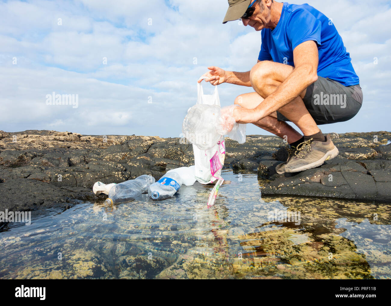 Un valore di Plogger/pareggiatore raccoglie rifiuti plastici dalla spiaggia rockpool durante la sua corsa mattutina Foto Stock