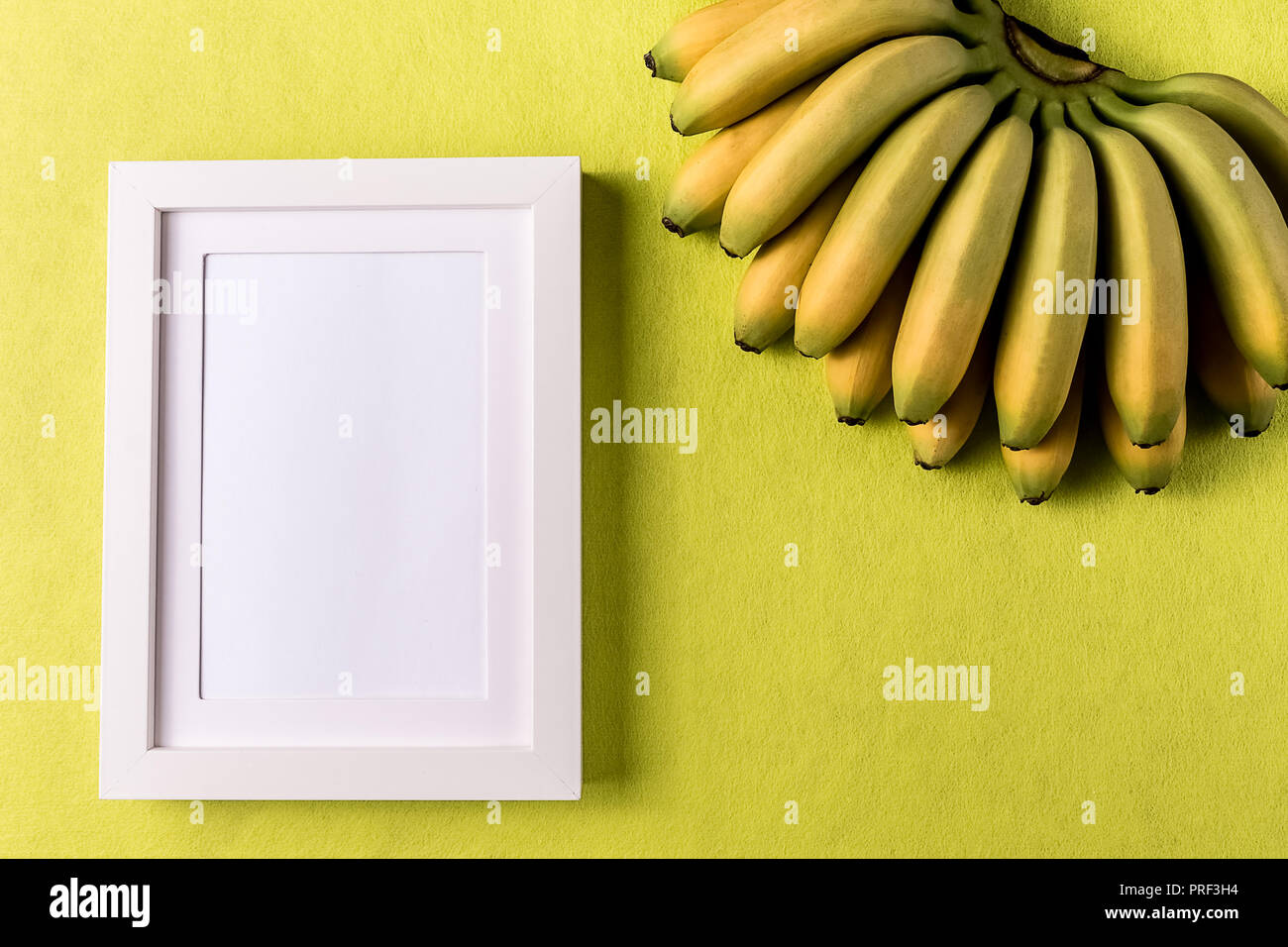 Stile minimalista. White empty picture frame e banana frutto contro abstract carta colorata copia di sfondo spazio, laici piana. Foto Stock