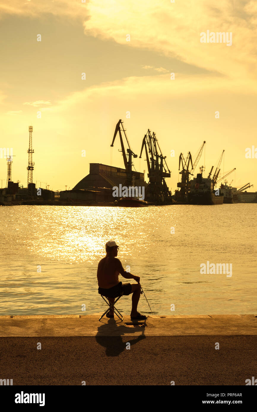 La Bulgaria,porto di Bourgas-pescatore la pesca nella zona industriale al tramonto Foto Stock