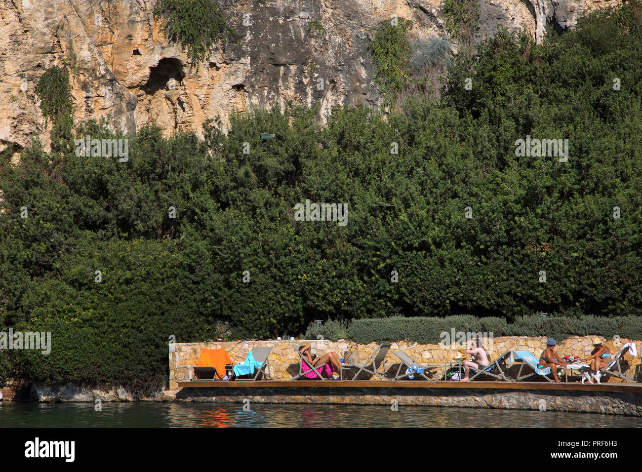 Vouliagmeni Atene Grecia turisti che prendono il sole sul lago Vouliagmeni una Spa naturale - una volta era una caverna, ma il tetto della grotta cadde in seguito all'erosione da t Foto Stock