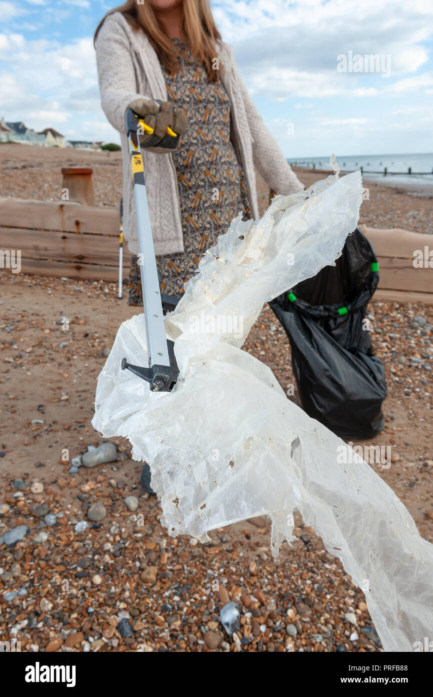 Una donna che preleva i rifiuti in plastica utilizzando un selettore di lettiera dalla spiaggia durante una comunità spiaggia pulita. Foto Stock