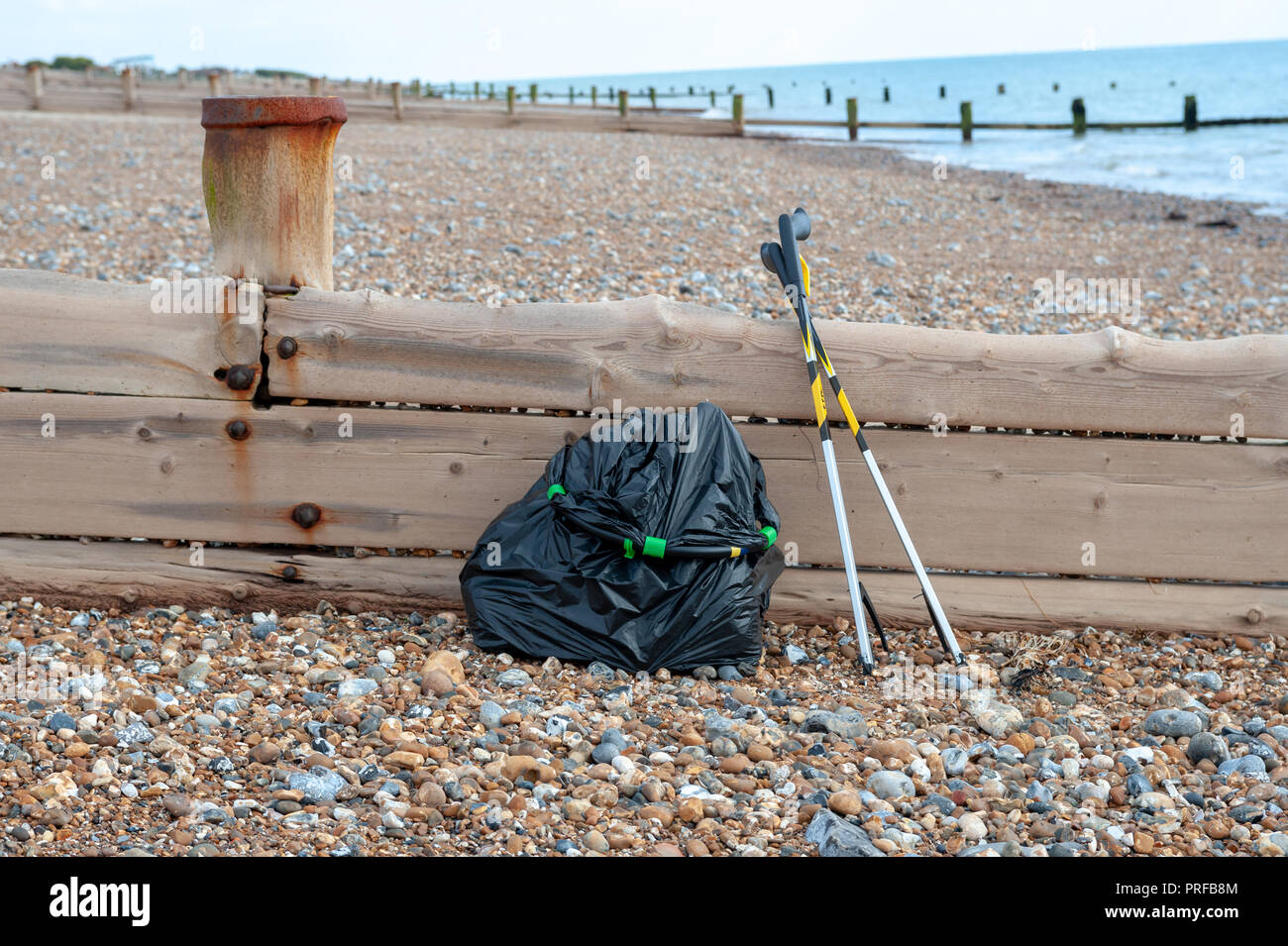 Spiaggia pulita. Una borsa nera piena di spazzatura raccolta dalla spiaggia e due lettiere pick up strumenti appoggiato su una tavola di legno groyne sulla spiaggia. Foto Stock