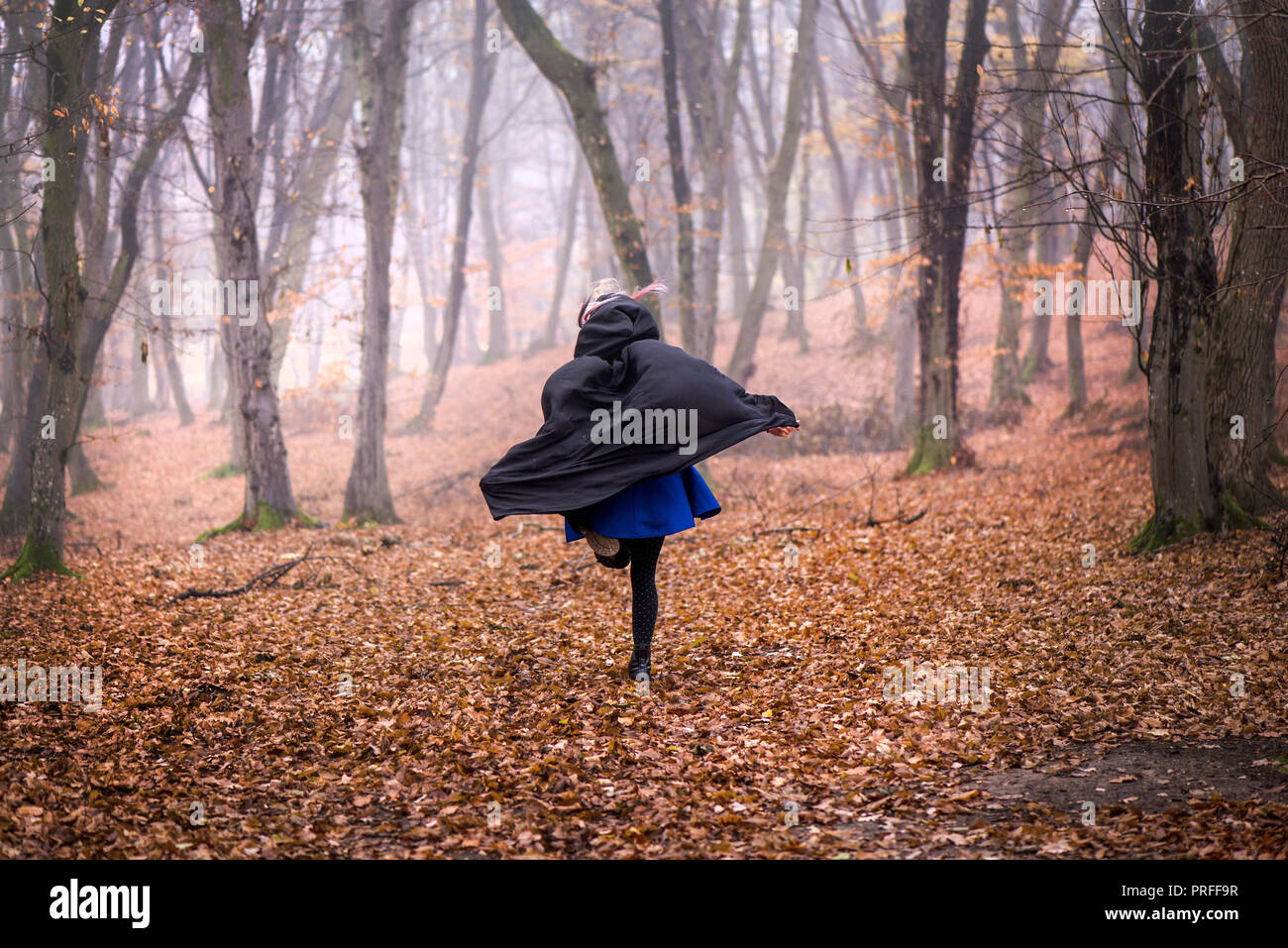 Ragazza in cappa nera di scappare dal pericolo nel profondo della foresta scura. Una fitta nebbia tutto intorno. Scary autunno scena Foto Stock