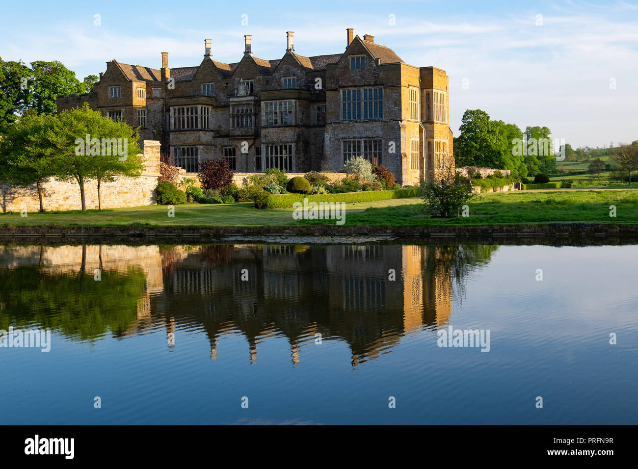 Castello di Broughton, vicino a Banbury, casa della famiglia Fiennes in golden luce della sera con riflessi nell'acqua ancora del fossato. Aperta al pubblico Foto Stock