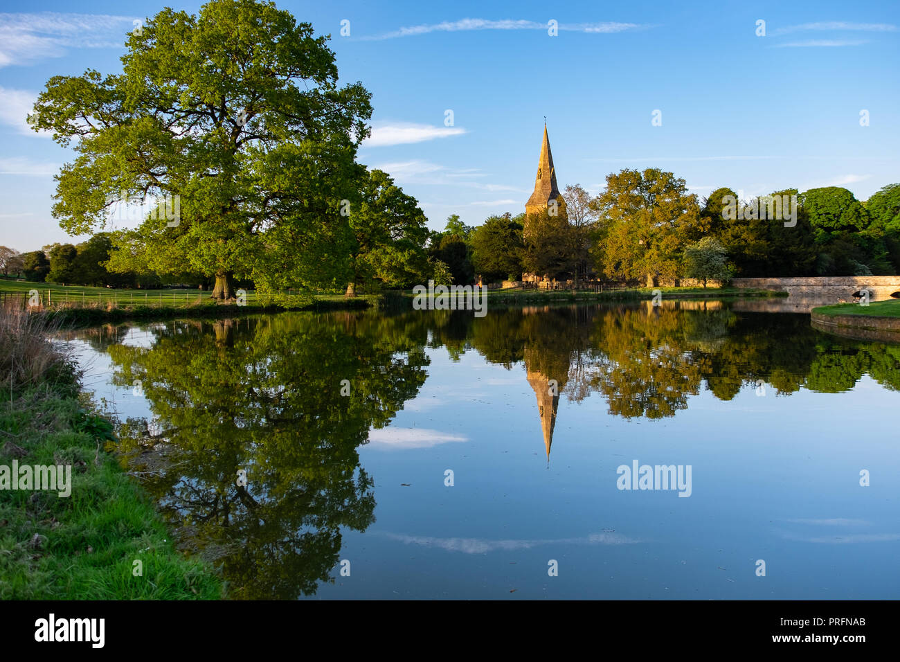 Castello di Broughton e chiesa, vicino a Banbury, casa della famiglia Fiennes in golden luce della sera con riflessi nell'acqua ancora del fossato. Foto Stock