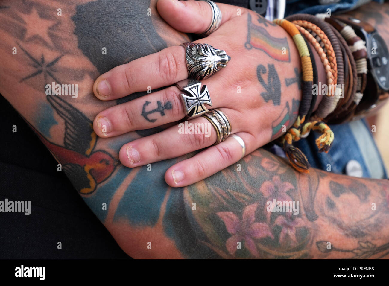 Fortemente e colorati tatuati lady la mano appoggiata sul suo braccio, indossando alcuni grossi anelli d'argento e legare i braccialetti di stile. Foto Stock