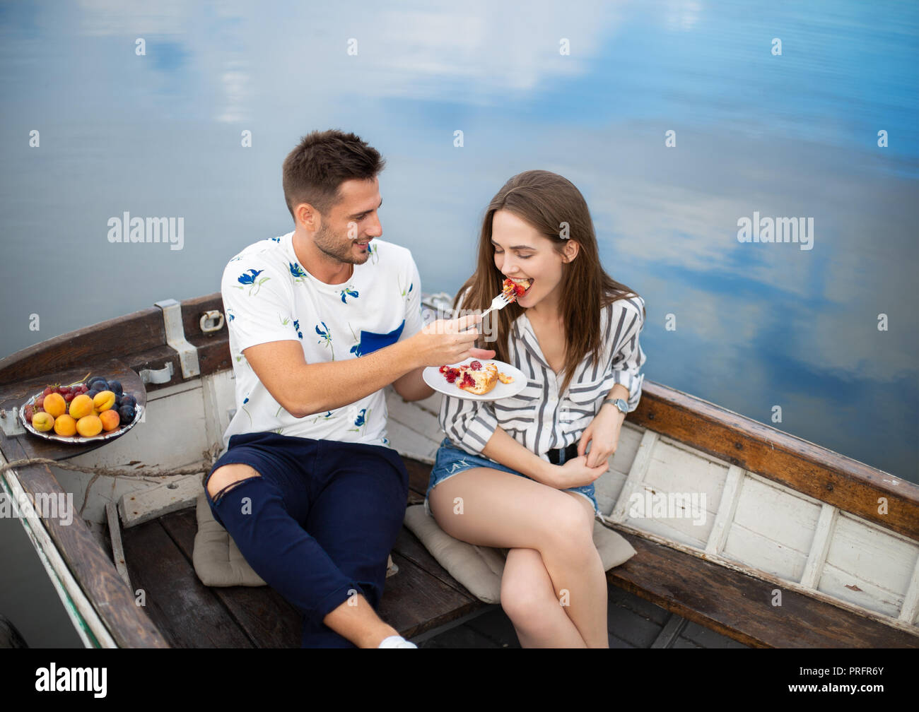Data romantico. L'uomo alimentando la sua ragazza seduta in barca nel fiume. Felice concetto di relazione Foto Stock