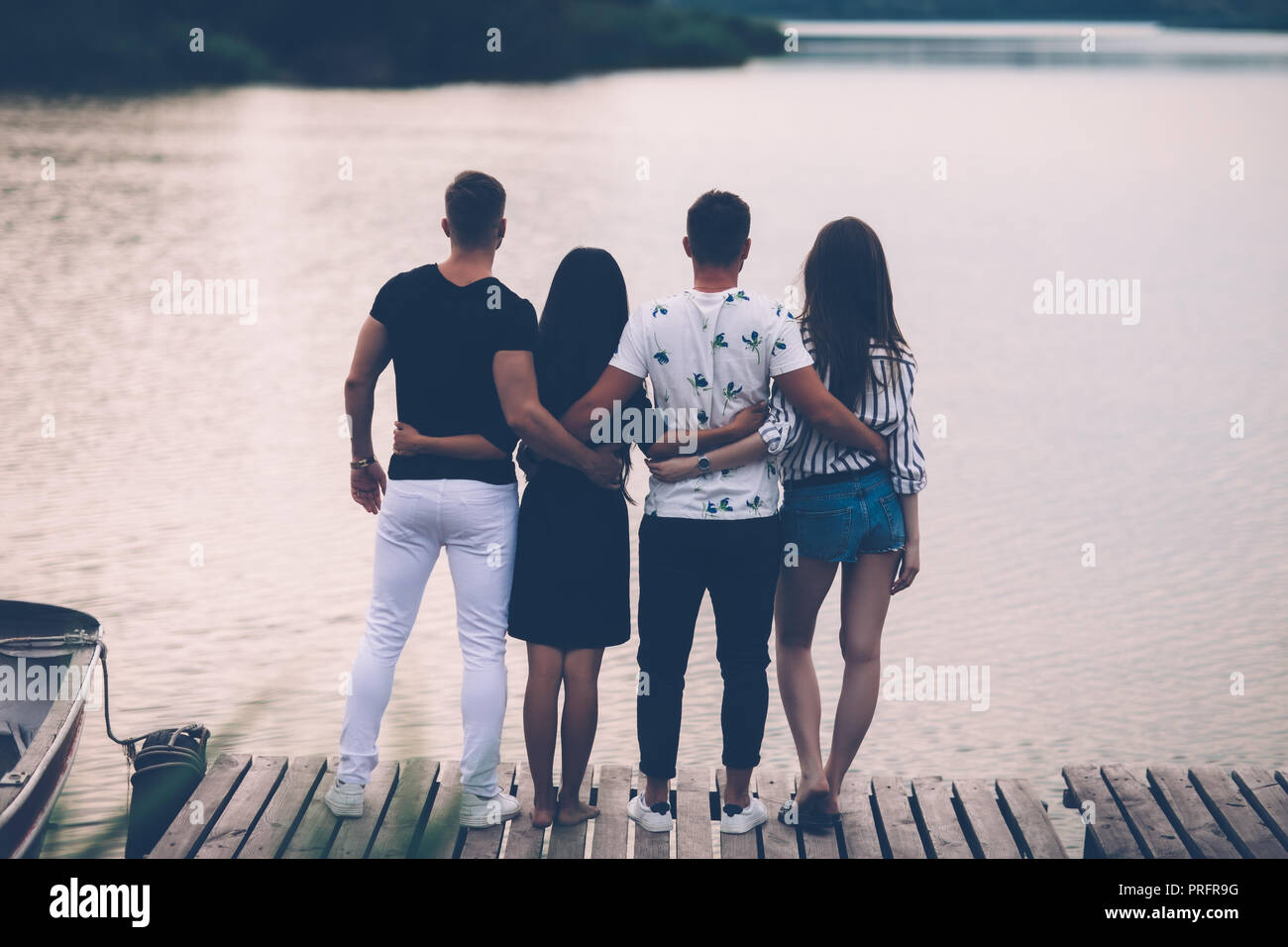 Vista posteriore di amici godersi il tramonto sul fiume in piedi sul molo in legno. Il concetto di amicizia Foto Stock