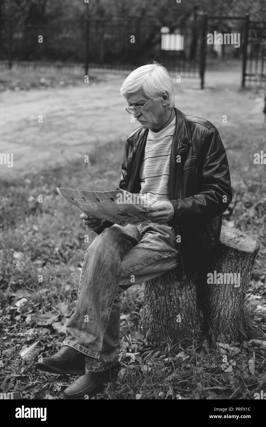 Un ritratto di un uomo grigio è di 60 anni. Egli tiene un giornale nelle sue mani. L'uomo ha scarsa capacità visiva, indossa gli occhiali Foto Stock