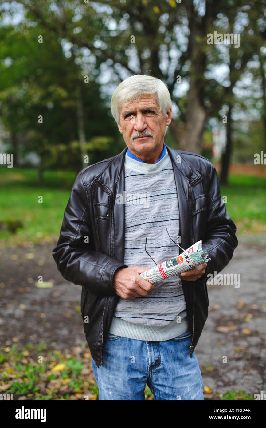 Un ritratto di un uomo grigio è di 60 anni. Egli tiene un giornale nelle sue mani. L'uomo ha scarsa capacità visiva, indossa gli occhiali Foto Stock