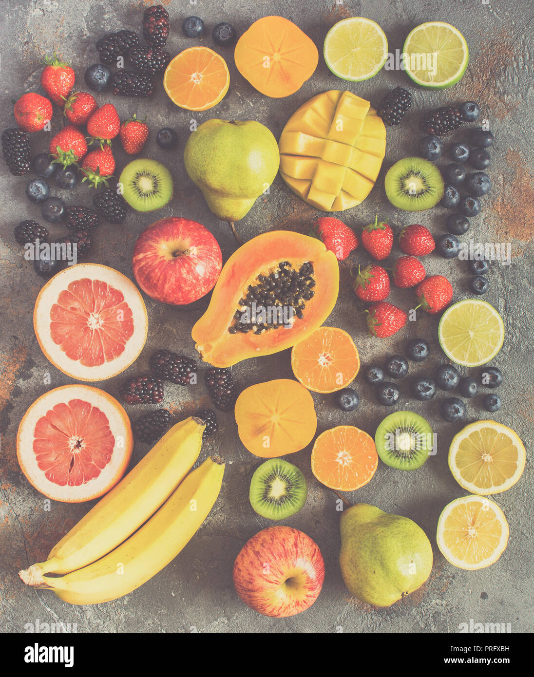 Diversi frutti arcobaleno, fragole, mirtilli, mango, arancia, pompelmo, banana, mela, uva da tavola, kiwi su sfondo grigio, vista sopra, tonica Foto Stock