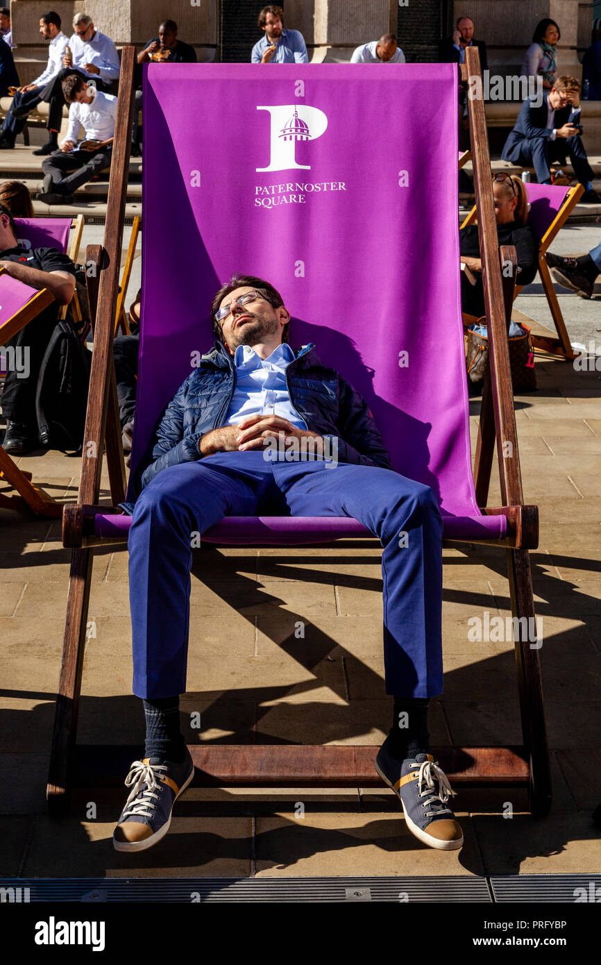 Un giovane uomo addormentato in una grande sedia a sdraio durante una pausa pranzo, Paternoster square, London, Regno Unito Foto Stock