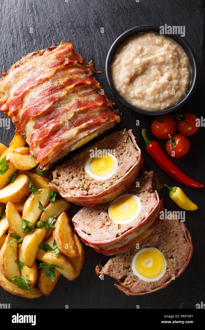Hackbraten pagnotta di carne con uovo servite con spicchi di patate e salsa di close-up su una piastra di ardesia sul tavolo. Verticale in alto vista da sopra Foto Stock