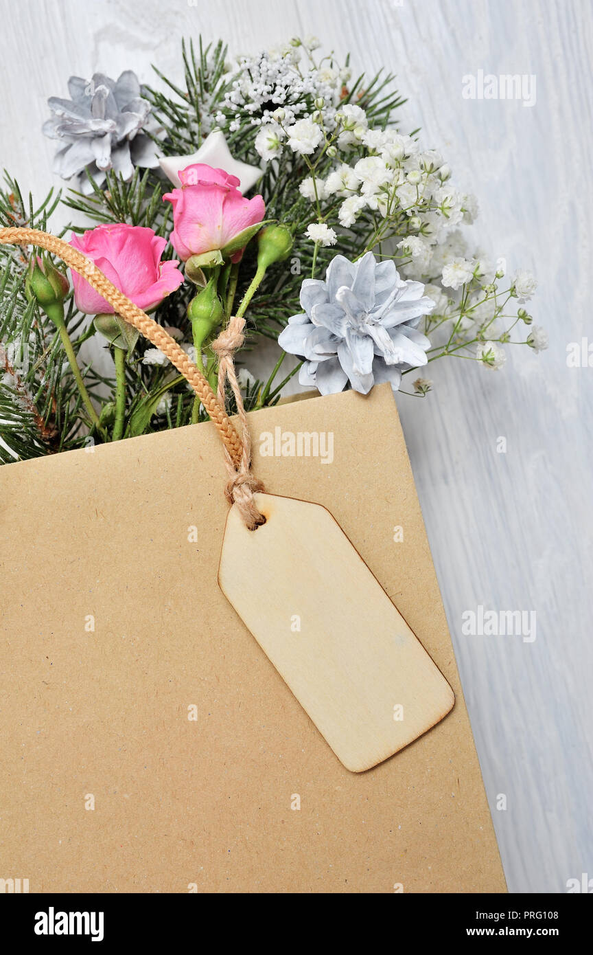 Natale mockup. Pacchetto Kraft con tag in legno e decorazioni di Natale Abete rami, le rose rosa, coni con posto per il vostro testo. Foto Stock