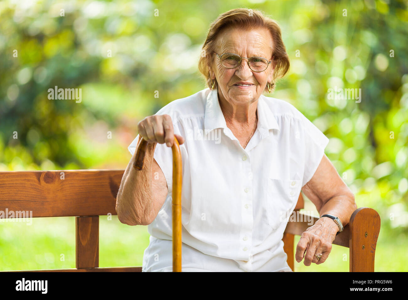 Donna anziana seduta e rilassante su un banco di lavoro all'aperto nel parco Foto Stock