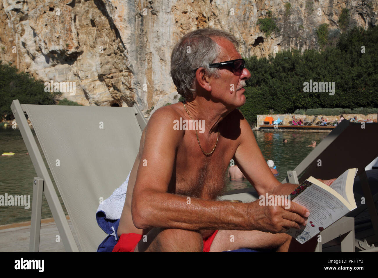 Vouliagmeni Attica Grecia Lago Vouliagmeni uomo la lettura di un libro su una sedia a sdraio Foto Stock