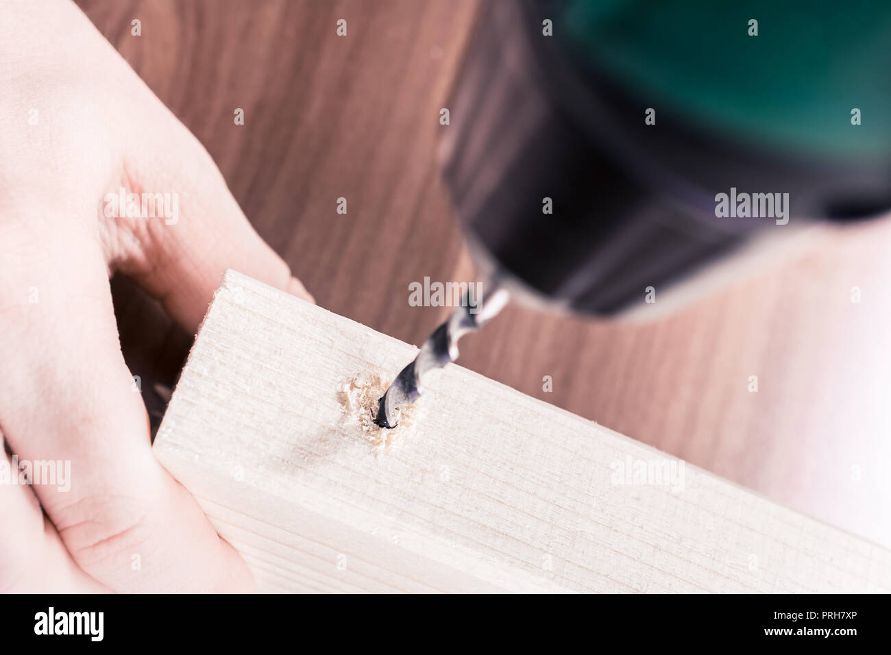 Artigiano tenendo in mano un pezzo di legno e utilizzando un trapano elettrico a praticare un foro in esso Foto Stock