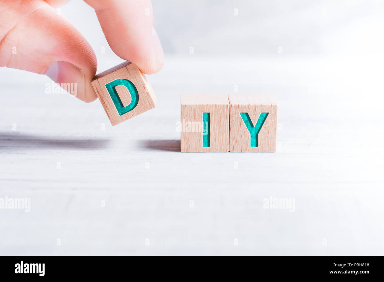 La sigla DIY formata da blocchi di legno e disposti a maschio le dita su un tavolo bianco Foto Stock