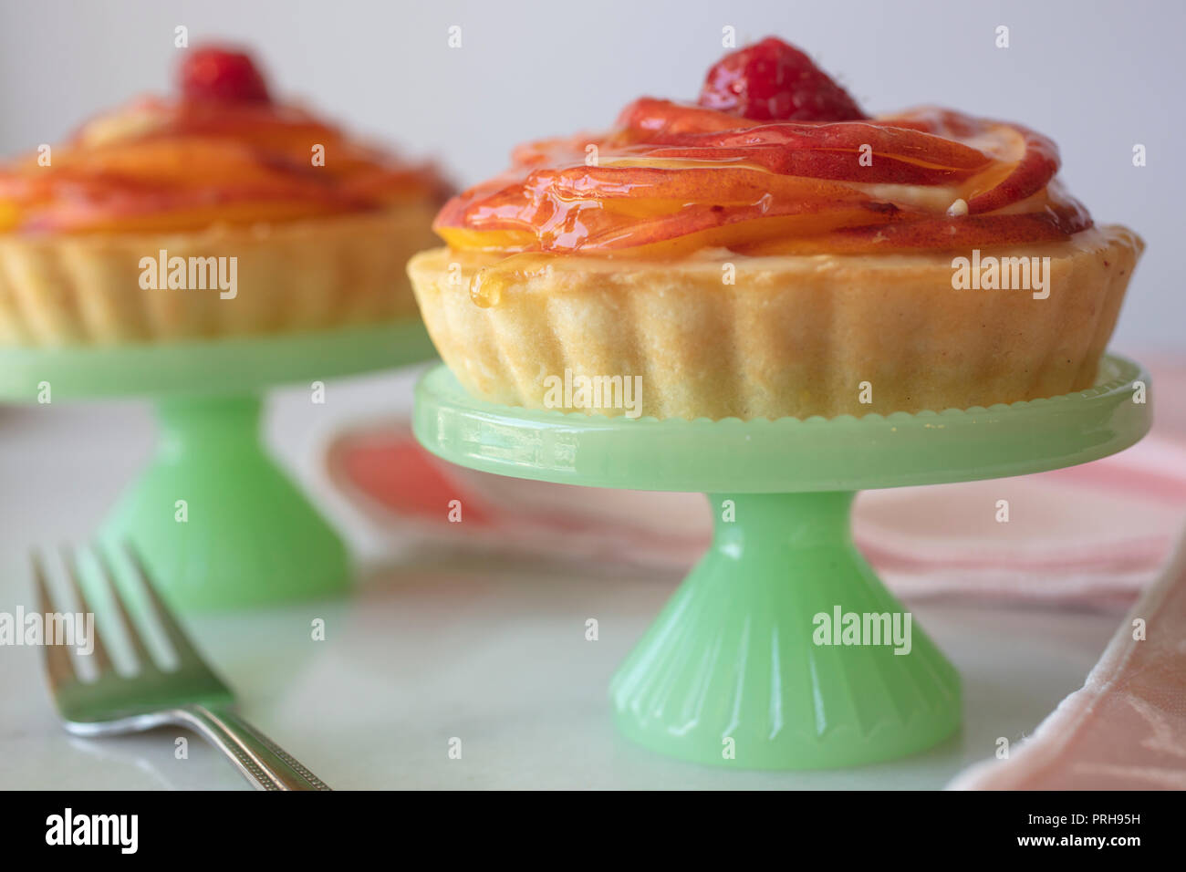 Stratificato in miniatura di pesche Tortino di crema con una crosta dorata e servita su un piccolo piedistallo piastra verde, rosa tovaglioli e forche Foto Stock