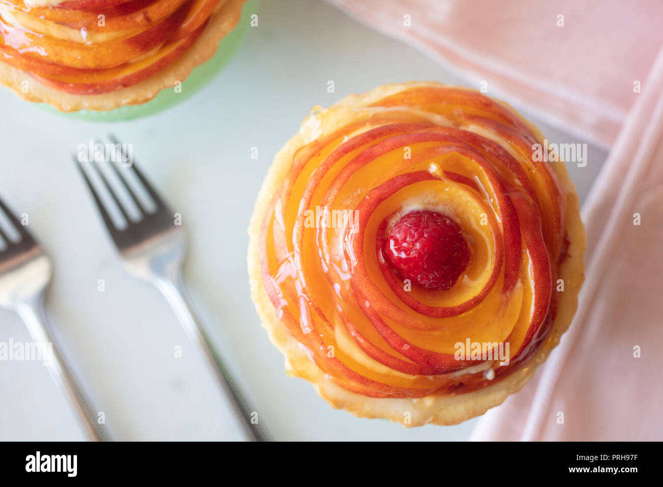 Stratificato in miniatura di pesche Tortino di crema con una crosta dorata e servita su un piccolo piedistallo piastra verde, rosa tovaglioli e forche Foto Stock