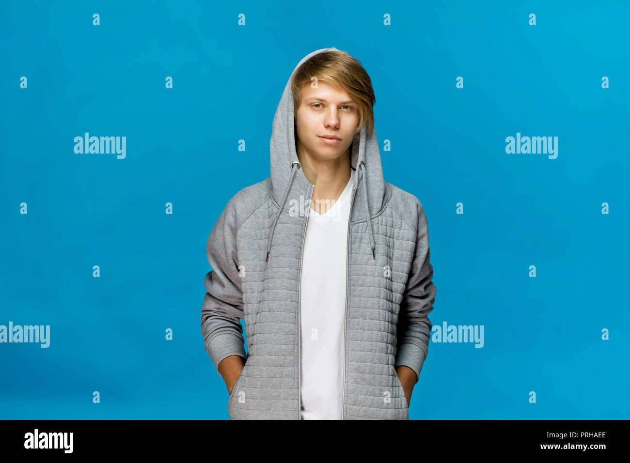 Allegro sorridente adolescente in grigio camicetta con la mano in tasca contro sfondo blu studio shot, isolato Foto Stock