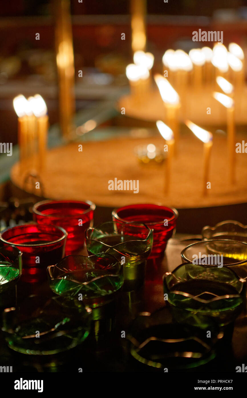 Veglia colorati bicchieri riempiti di olio in una chiesa ortodossa orientale con acceso candele votive. Foto Stock