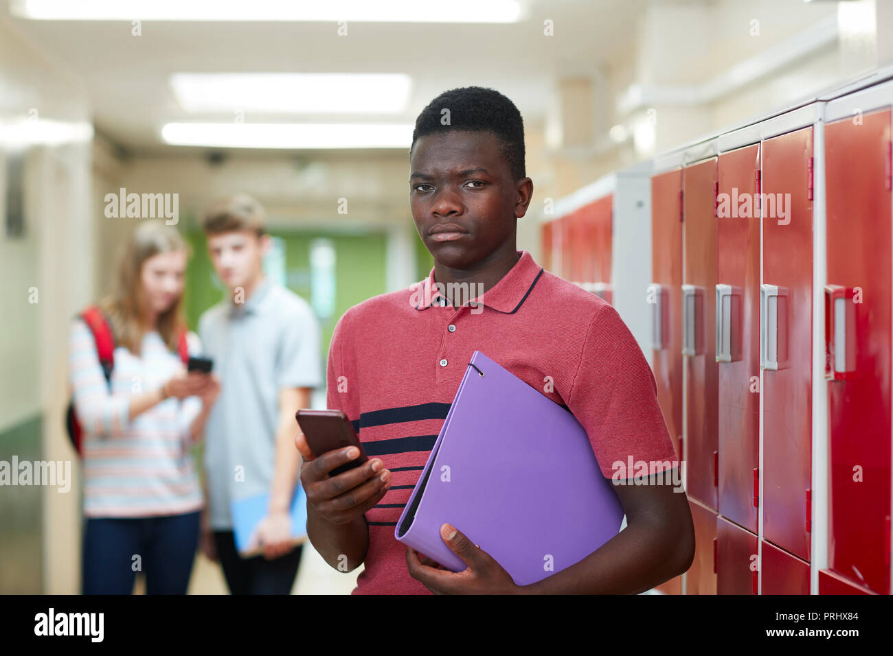 Ritratto maschile di alta scuola studente intimorito da un messaggio di testo in corridoio Foto Stock