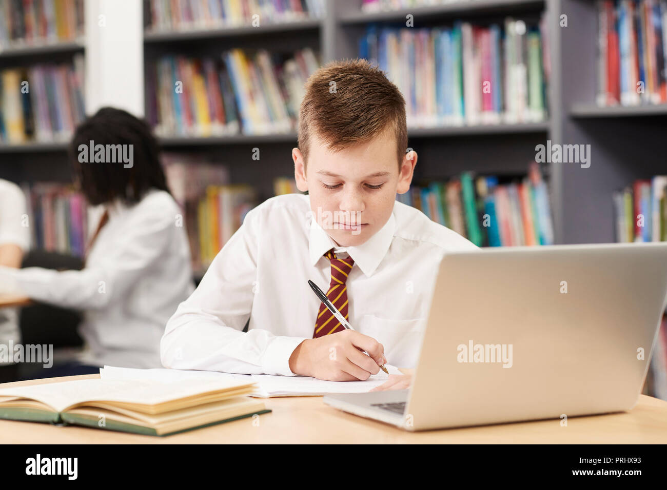 Maschio di studente di scuola superiore che indossano uniformi di lavorare al computer portatile in biblioteca Foto Stock