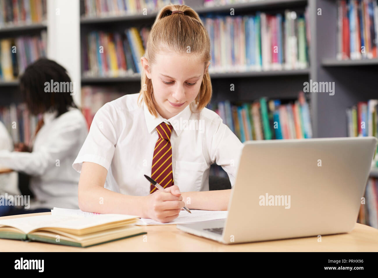 Femmina di studente di scuola superiore che indossano uniformi di lavorare al computer portatile in biblioteca Foto Stock