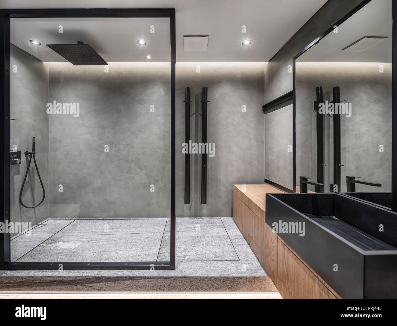 Bagno in stile moderno con tonalità grigio pareti piastrellate. C'è una doccia con una parete di vetro, supporto di legno nero con un lavandino e un rubinetto, specchio di grandi dimensioni, Foto Stock